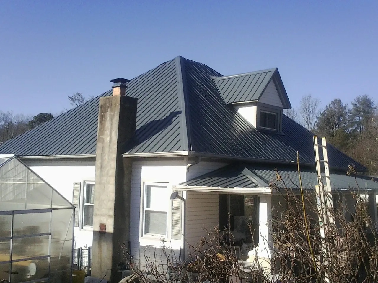 Dark blue standing seam metal roof on a white farmhouse with dormer — Slate & Tile Roof Repair by Roofing Brothers in Vance
