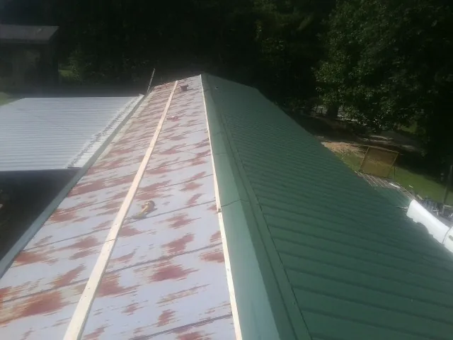 Old rusted panels beside newly installed green metal roofing — Wind Damage Roof Repair by Roofing Brothers in Vance